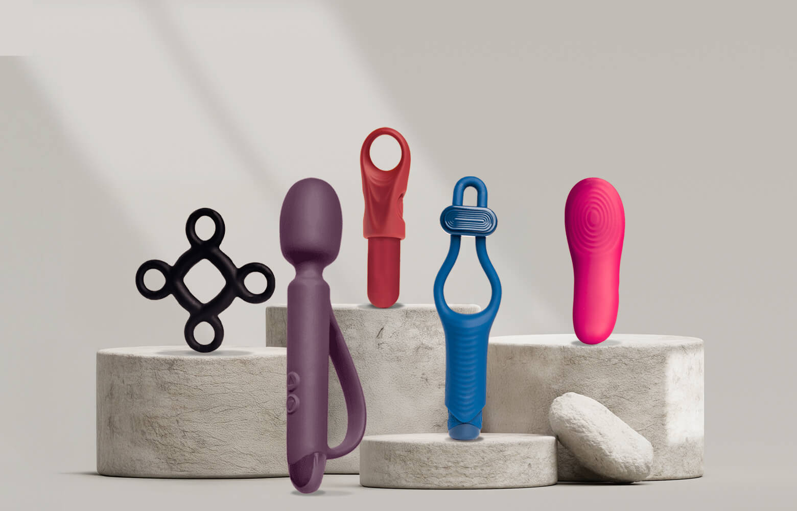 Collection of quest products on a stone podium including a wand, c-ring and panty vibe