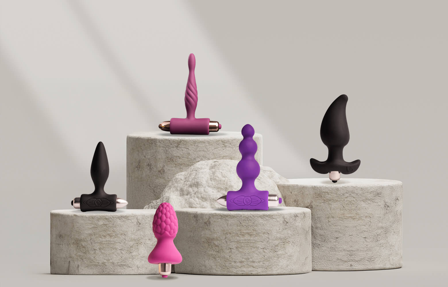 Collection of various vibrating butt plugs on a stone podium in different colours and sizes