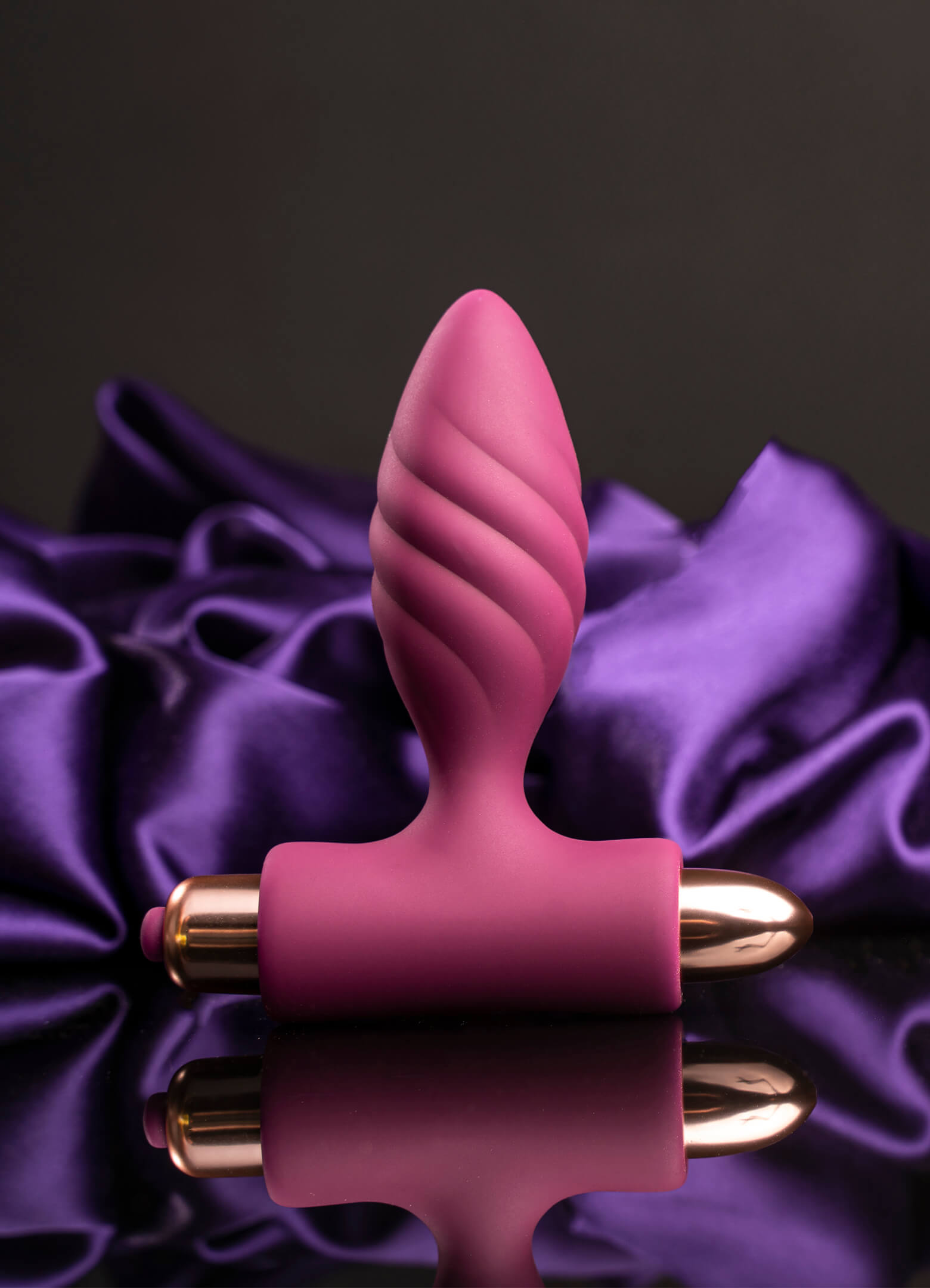 Silicone burgundy butt plug with a twisted ribbed head housing a rose gold removable bullet vibrator.