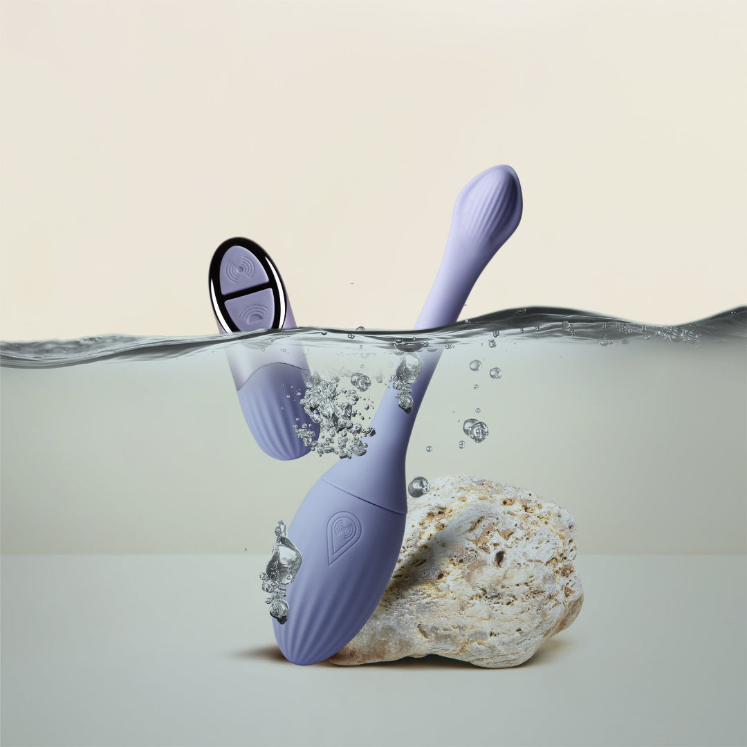 A lavender purple underwater NIYA N1 with a matching remote, partially submerged in water next to a white rock, set against a clean beige background. waterproof design