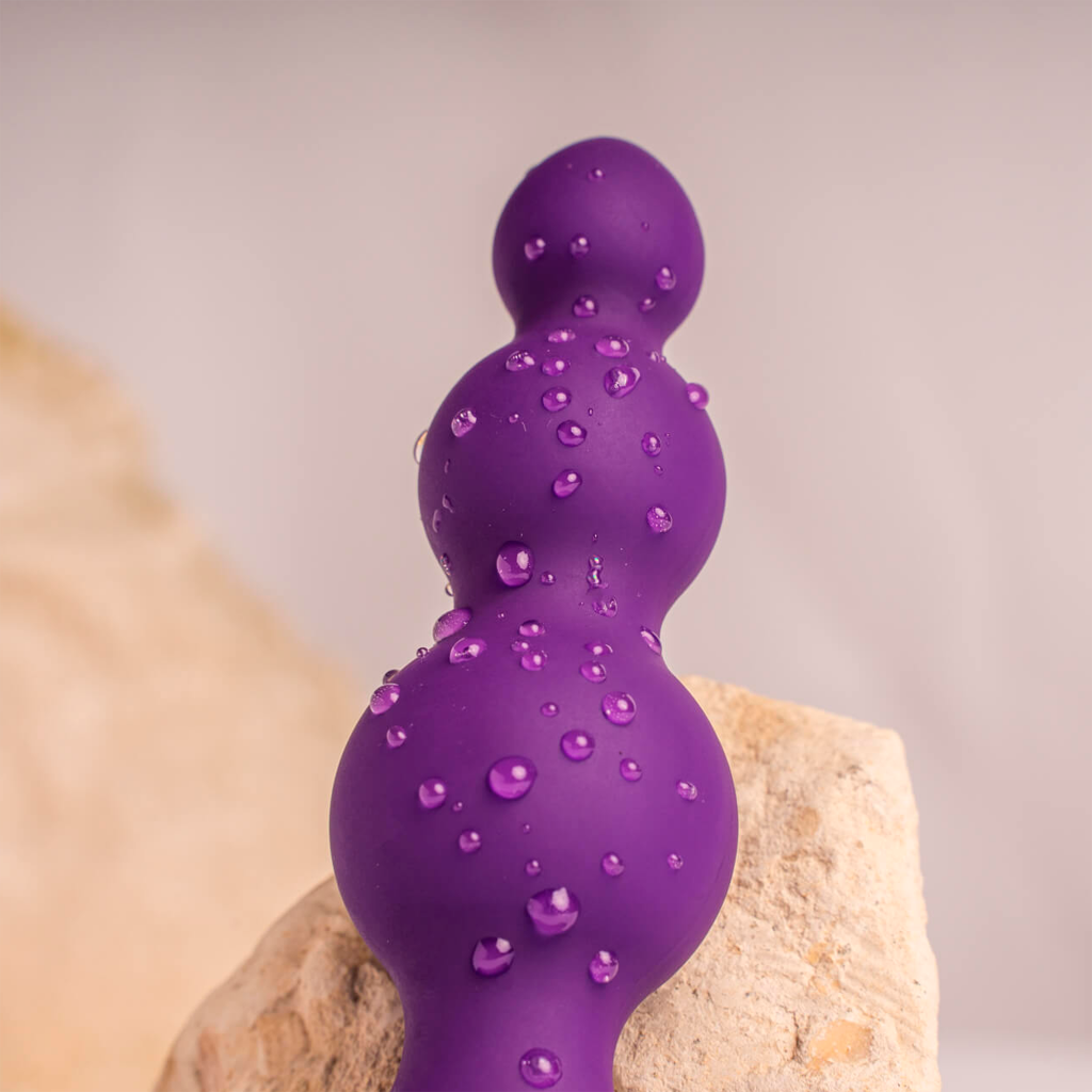 Purple silicone vibrating anal beads with three rounded tips, covered in water droplets