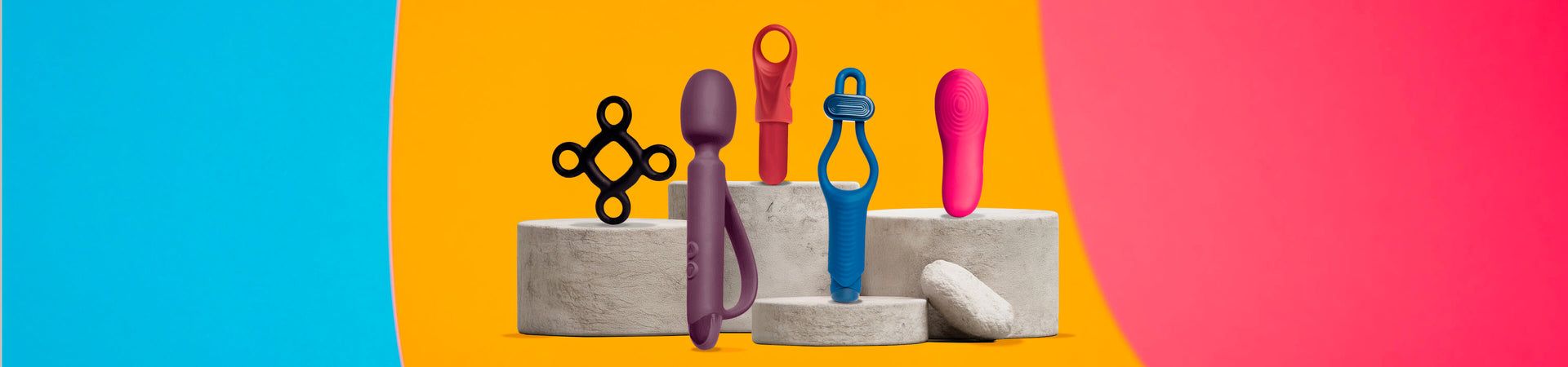 Collection of quest product a stone podium including a wand, c-ring and panty vibe with a bright colourful background