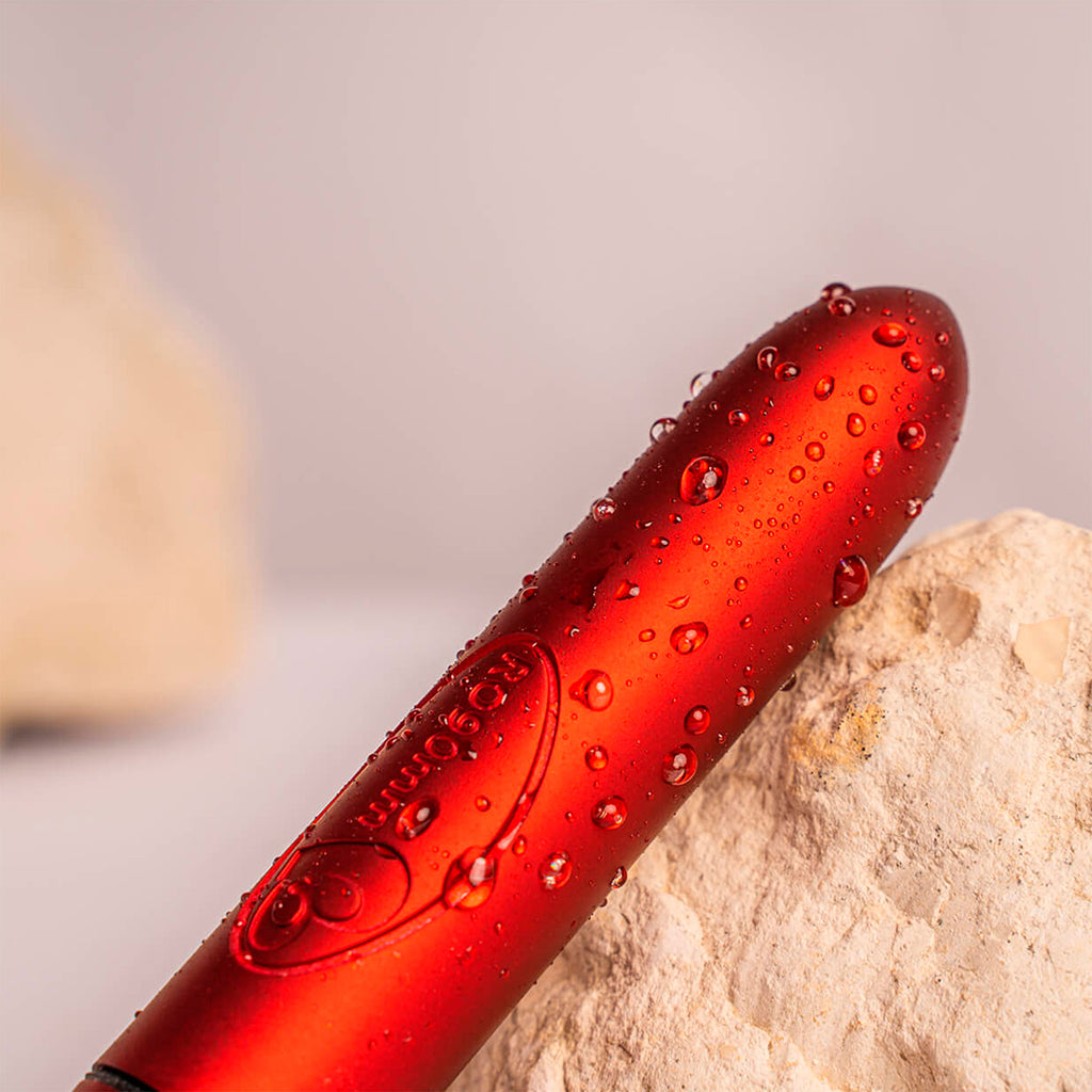 Scarlet Velvet bullet vibrator, product shown laying on a rock and beaded in water droplets to show it is waterproof.