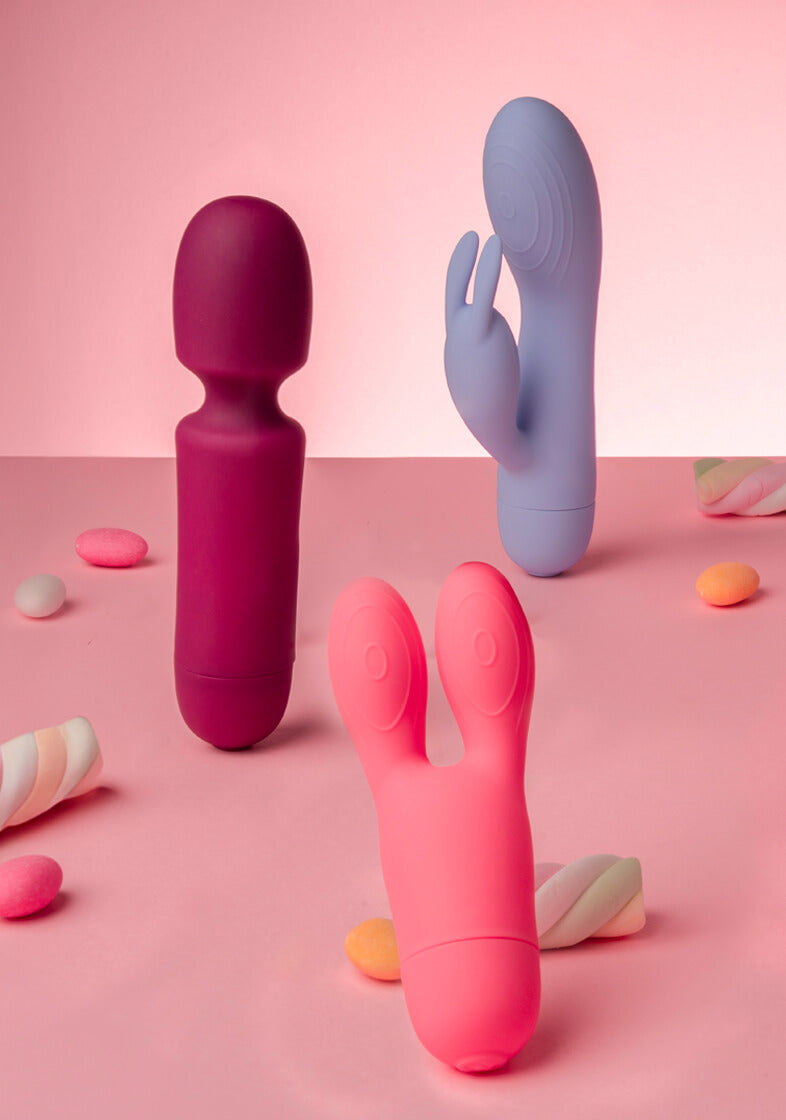collection of sugarboo products against pink background with sweets including rabbit vibrator, mini wand,  and bunny vibrator mobile version