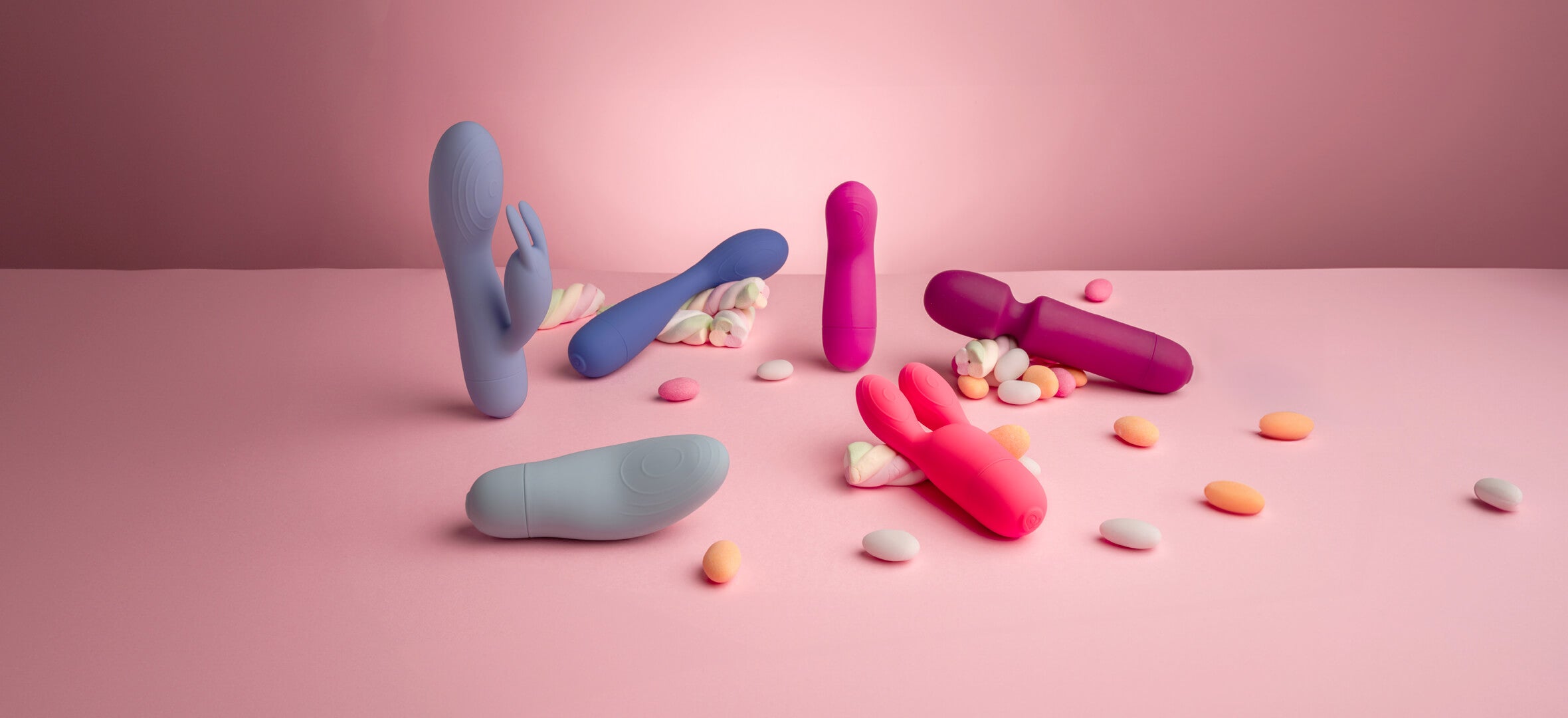 collection of sugarboo products against pink background with sweets including rabbit vibrator, mini wand, massager and bunny vibrator