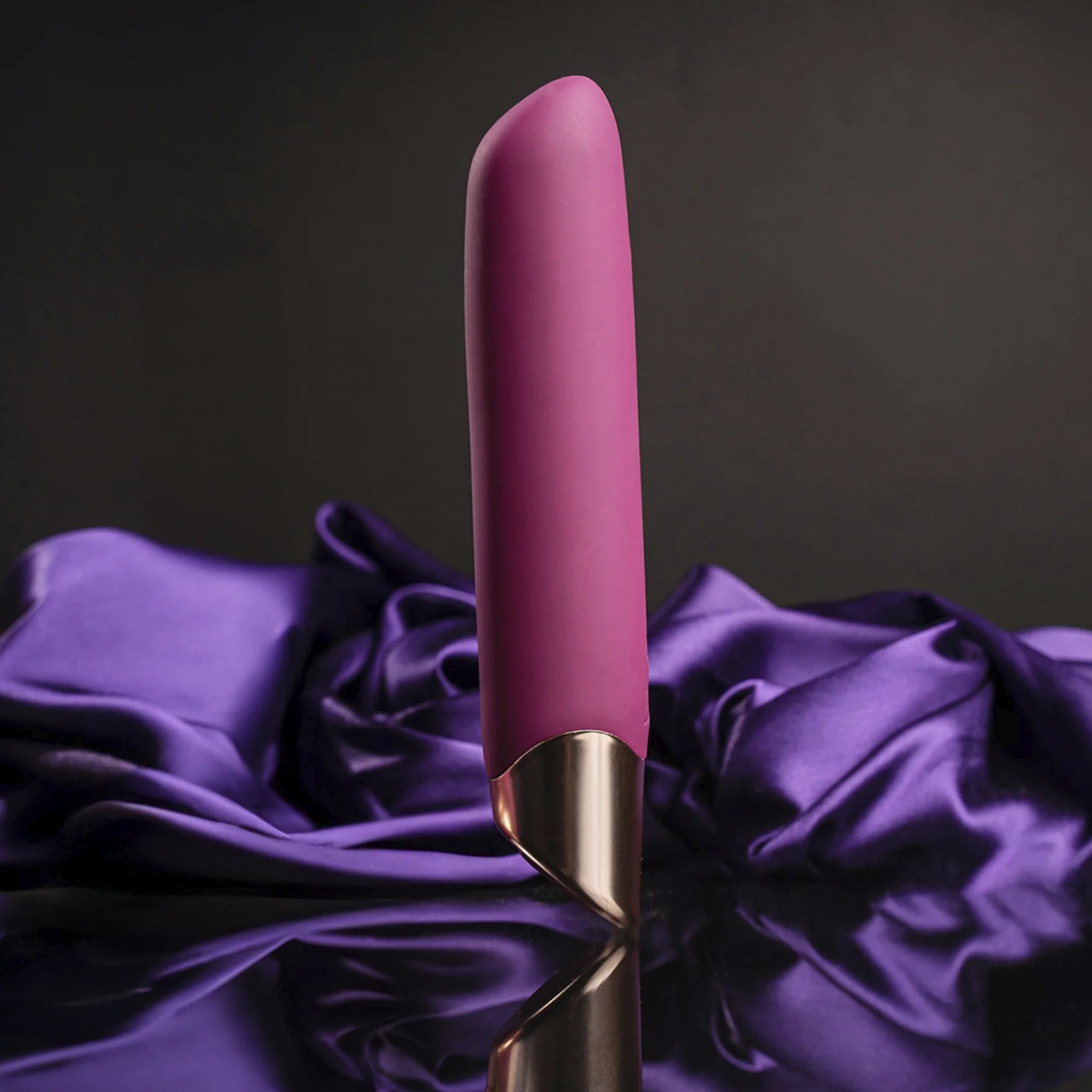 Magenta-purple vibrator wand with metallic base resting on wrinkled fabric.