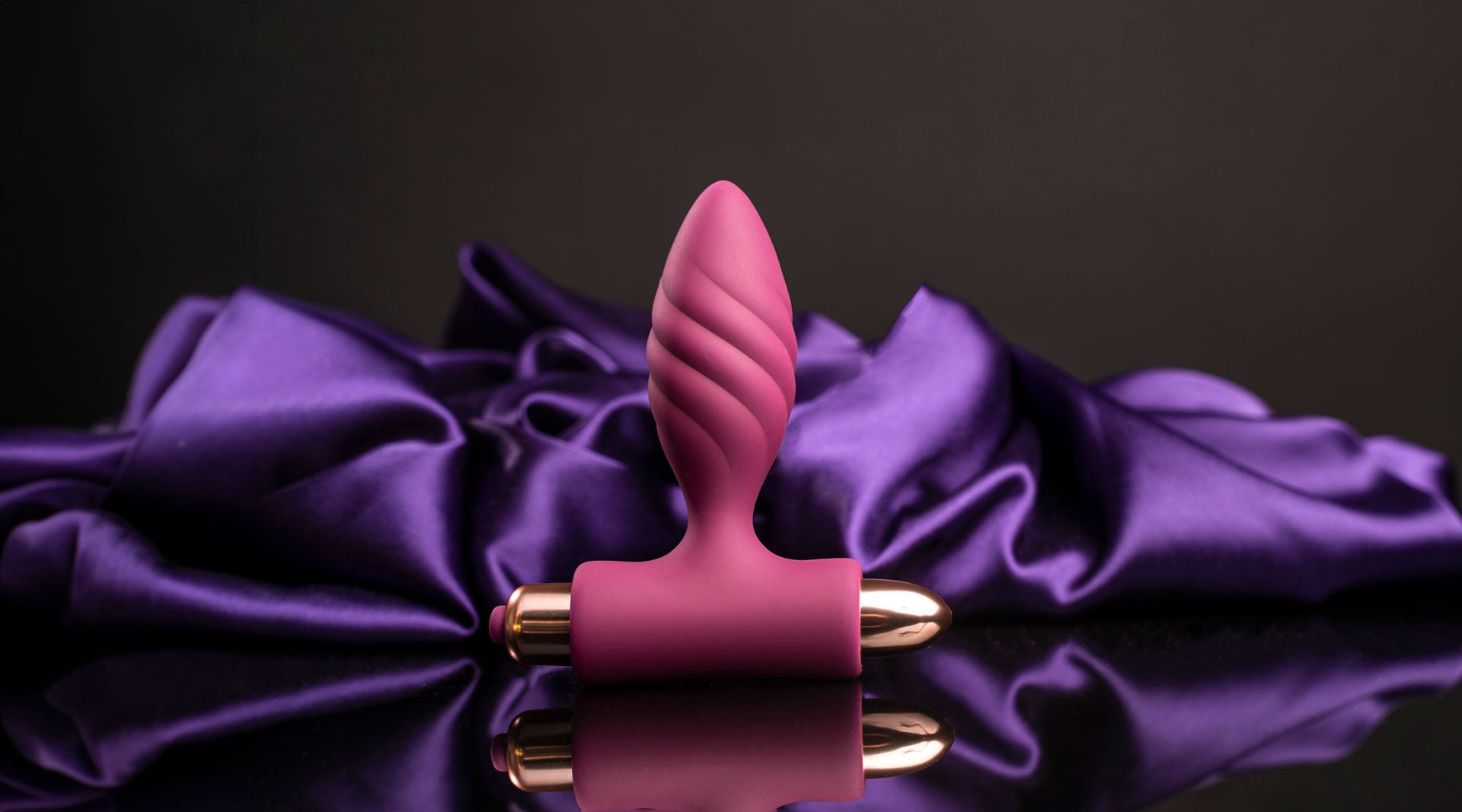 Silicone burgundy butt plug with a twisted ribbed head housing a rose gold removable bullet vibrator.