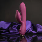 Bright pink rabbit-style massager standing upright on purple satin fabric