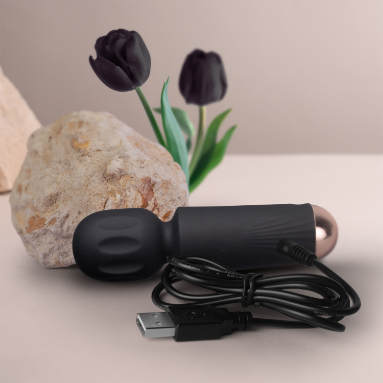 Black mini wand vibrator with oval head and USB charging cable on stone