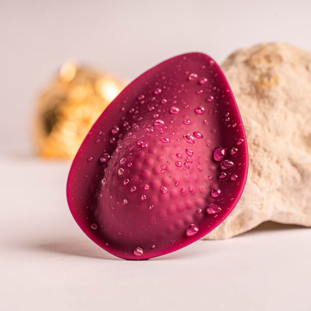 Maroon silicone teardrop massager with water droplets on textured surface