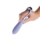 A hand holding a lavender purple Niya Finger Vibe with a curved silicone body and a metallic silver loop handle, set against a plain white background.