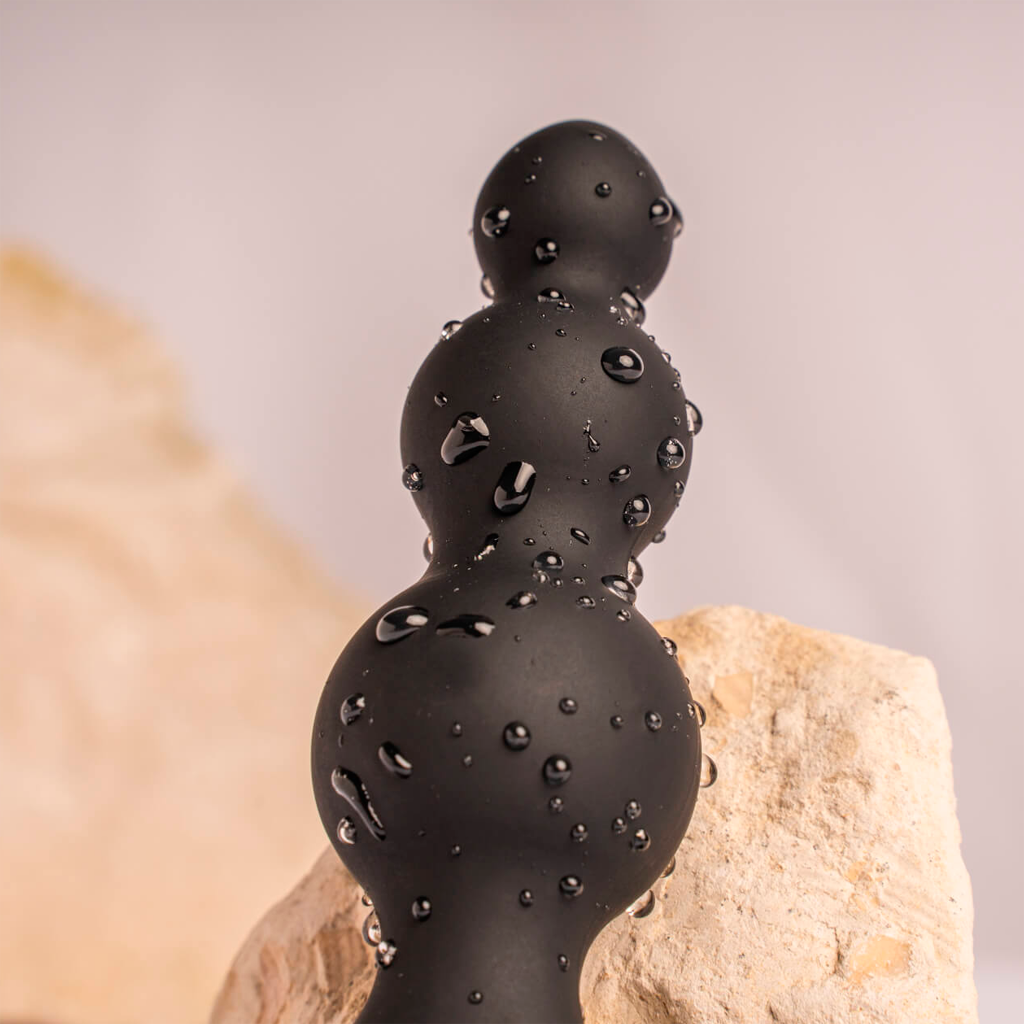 Black silicone vibrating anal beads with three rounded tips, covered in water droplets