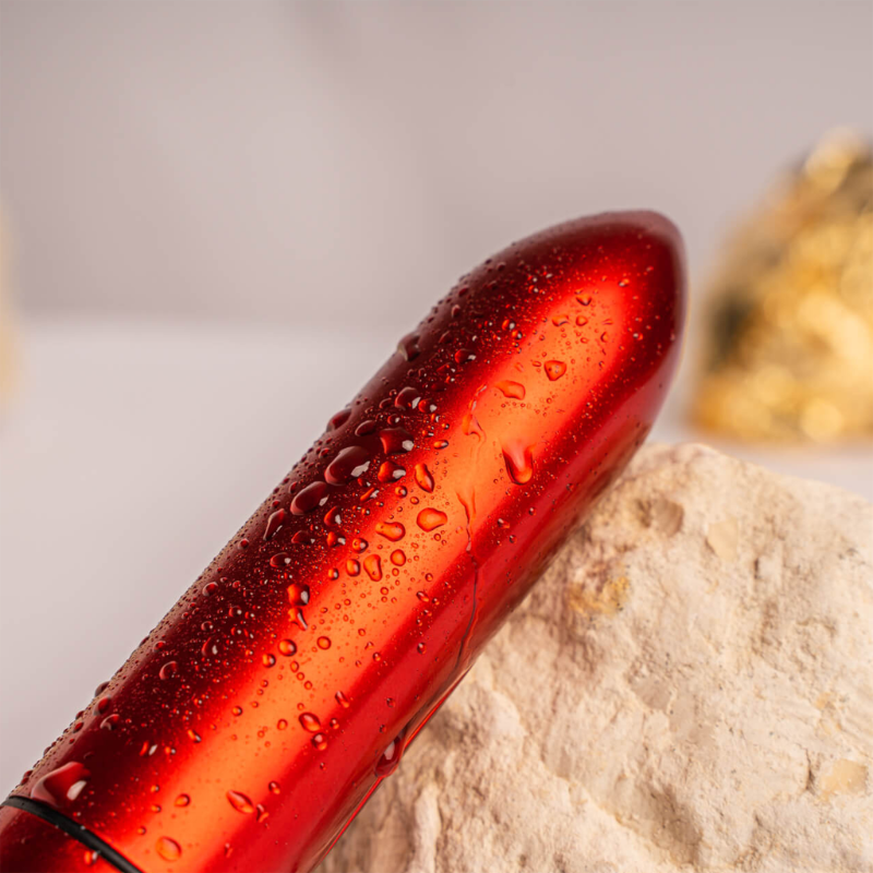Red bullet-shaped device with water droplets on the metallic surface