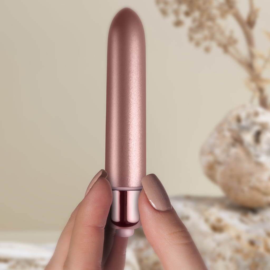 Rose gold bullet vibrator with glossy metal base, held in two fingers