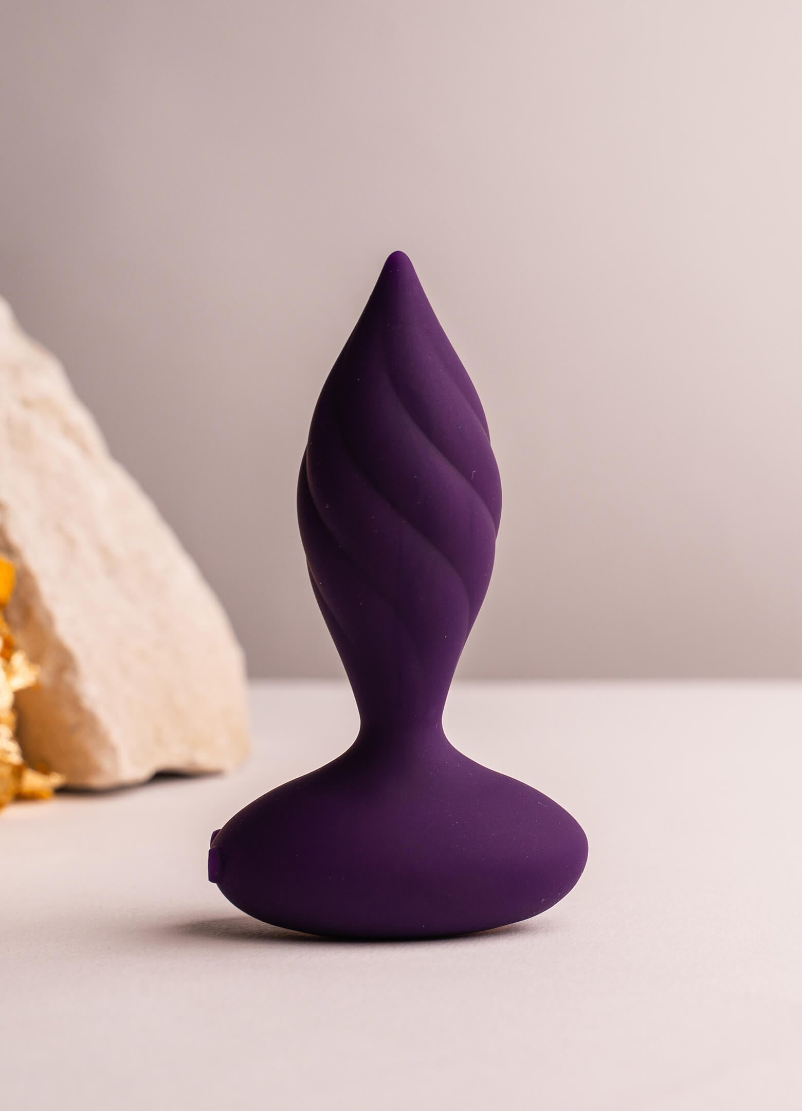 Purple silicone butt plug with a tapered tip and twisted surface design.