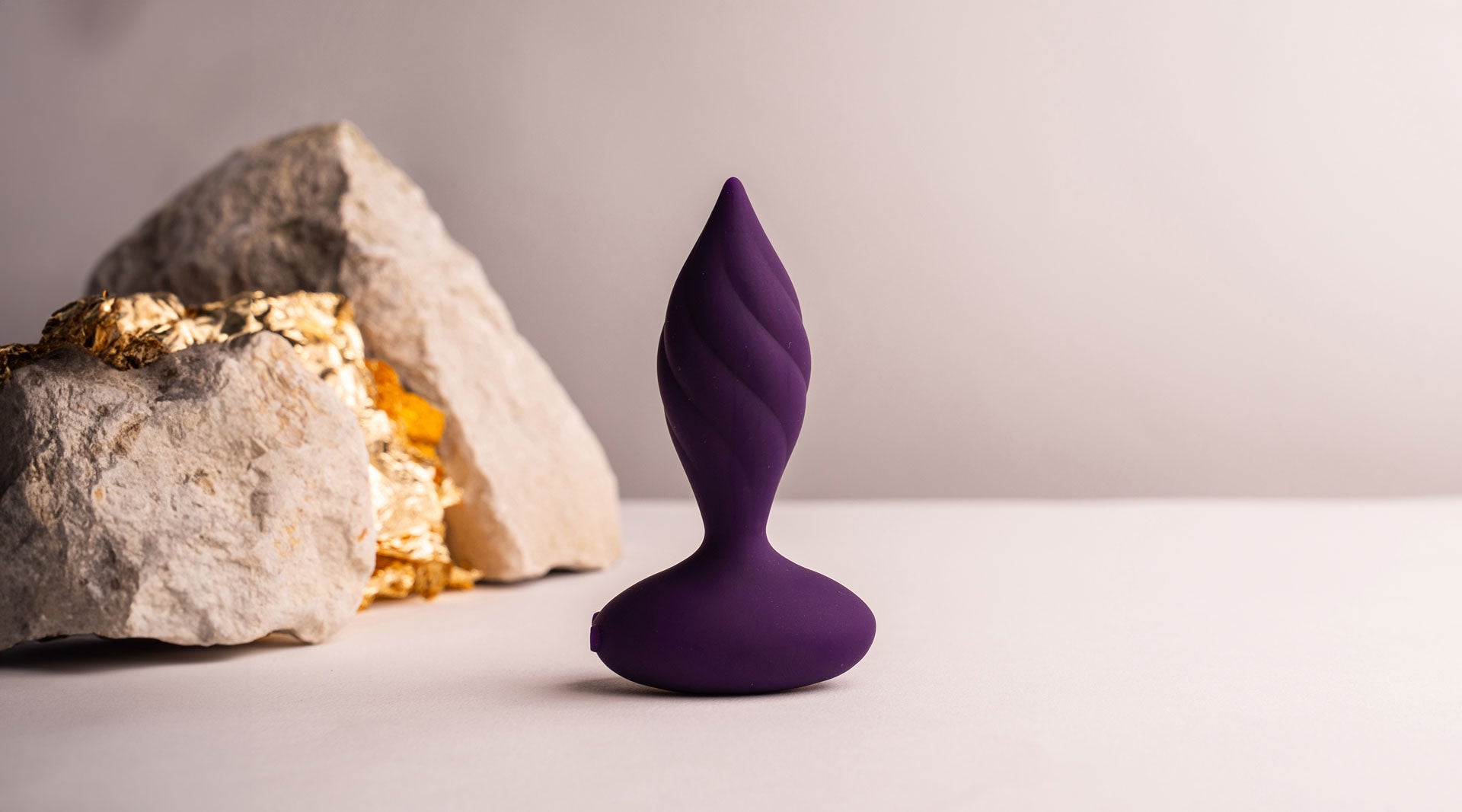 Purple silicone butt plug with a tapered tip and twisted surface design.