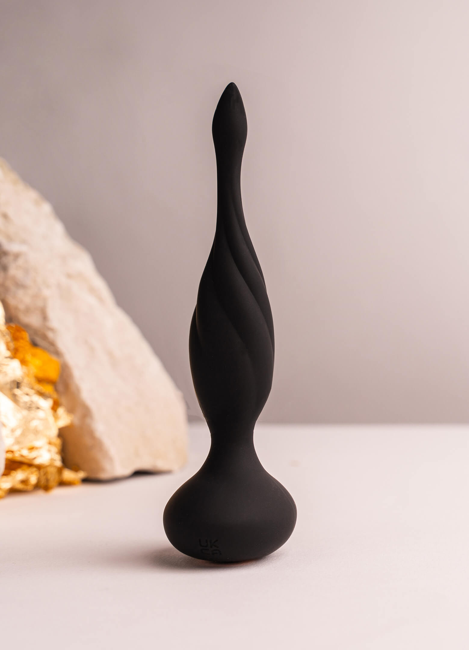 Thin tipped black silicone butt plug with a twisted surface design.