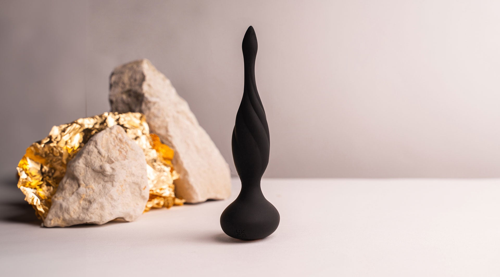 Thin tipped black silicone butt plug with a twisted surface design.