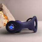 A dark purple Zenturian with an integrated blue LED light, resting on a neutral surface with a blurred decorative rock in the background