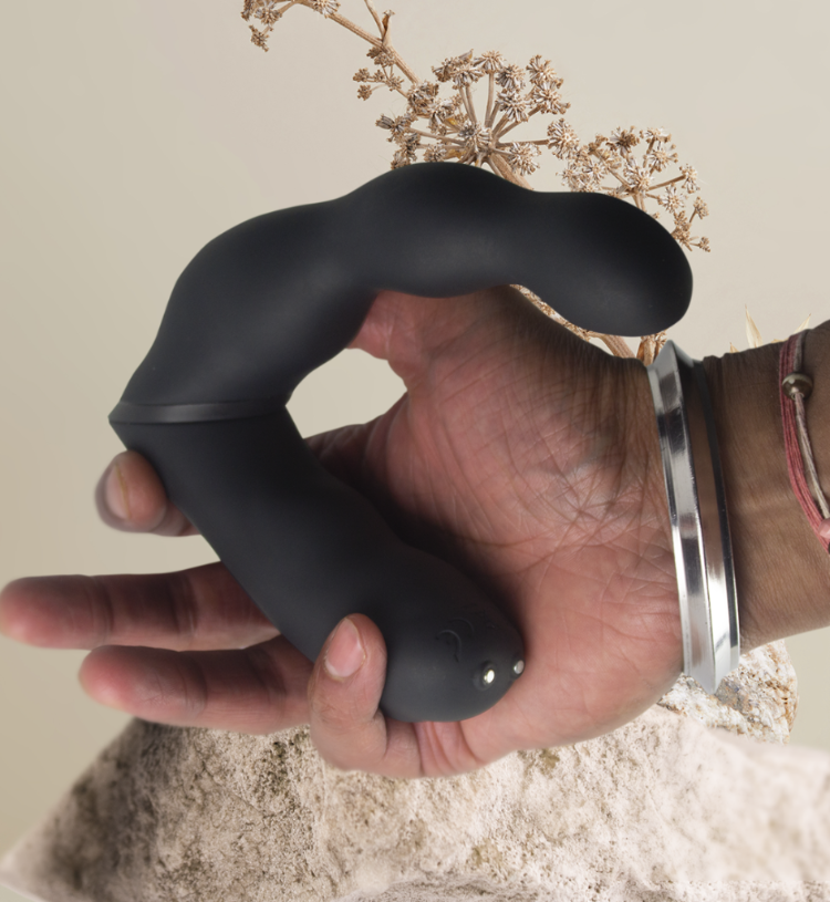 Black dual-motor prostate and anal massager held in hand, showing control dots