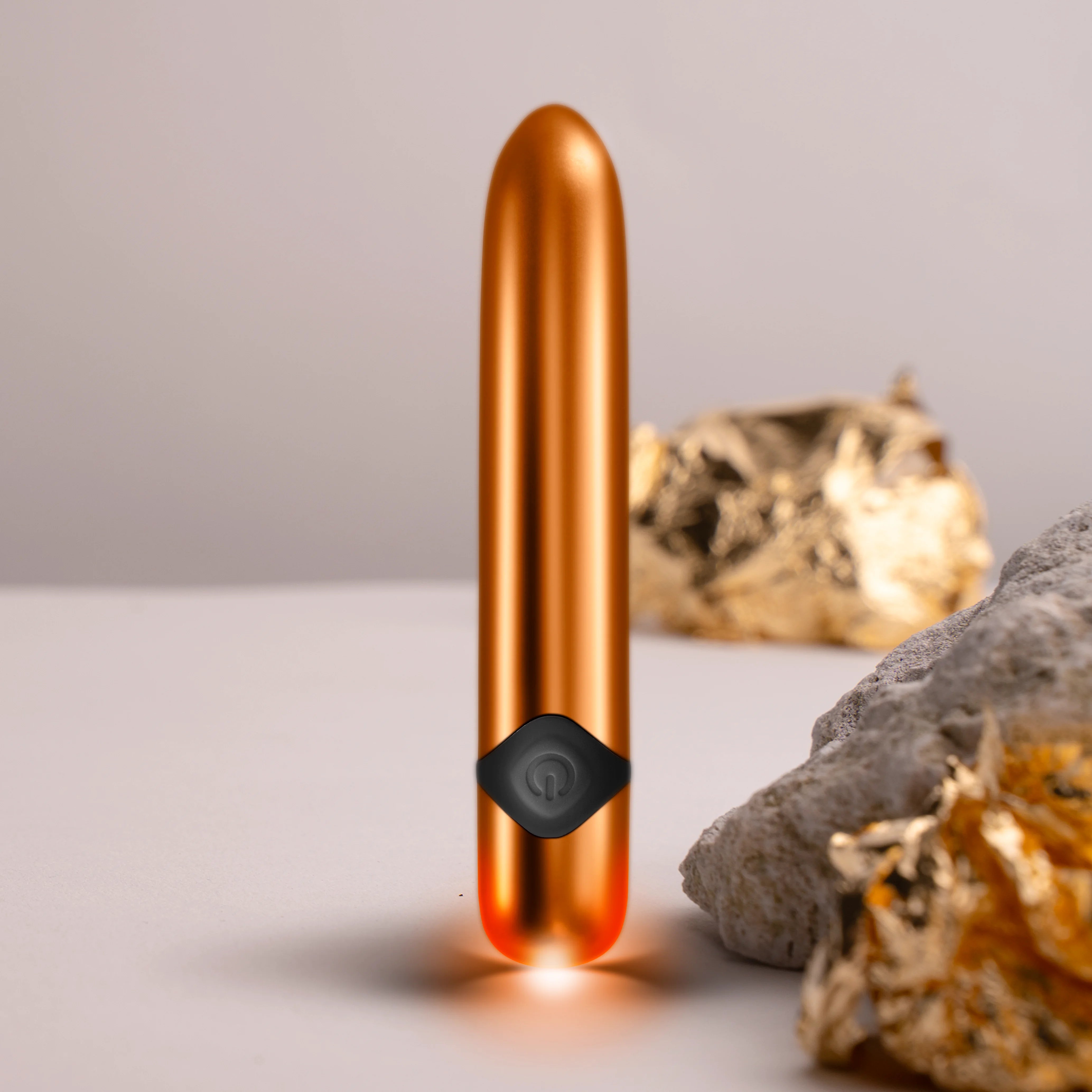 Havana orange metallic massager wand standing upright on rocky surface, black cap