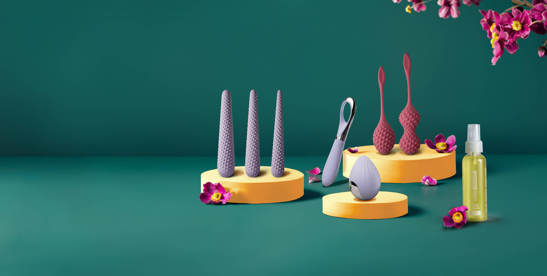 Silicone Kegels, dilators and lube on orange podiums surrounded by pink flowers on a teal background