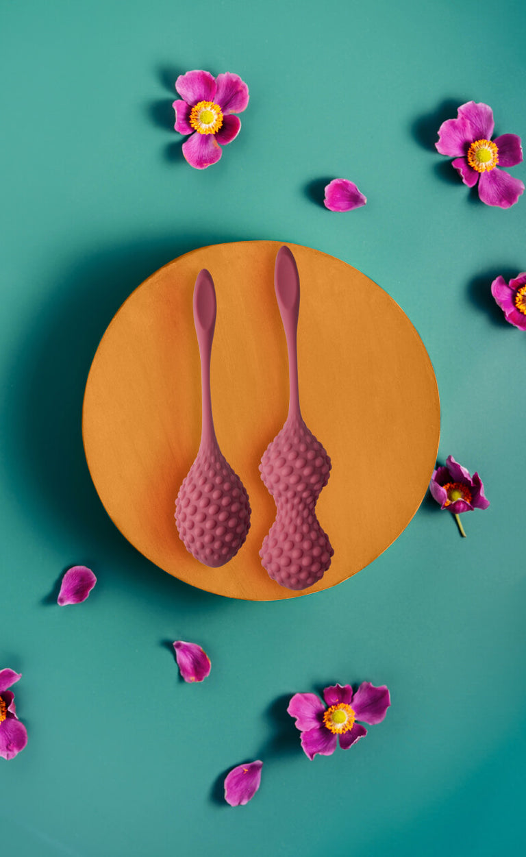 Silicone Kegels on orange podium surrounded by pink flowers on a teal background